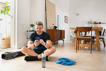 Een man in sportkleding zit op de grond met zijn smartphone in handen. 