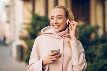 Vrouw heeft AirPods in haar oor en een smartphone in handen