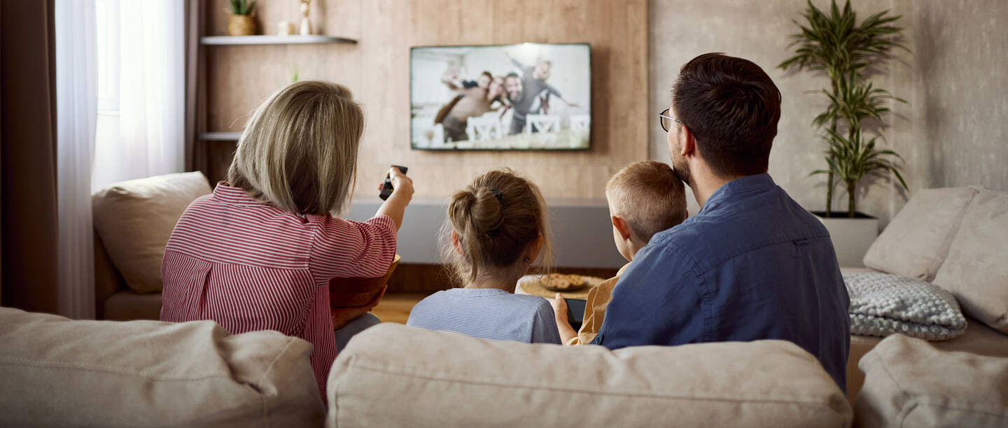 Je ziet een gezin van achteren, zittend op een bank en samen tv kijkend