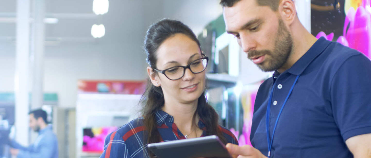 Een verkoopmedewerker bekijkt een tablet met een klant