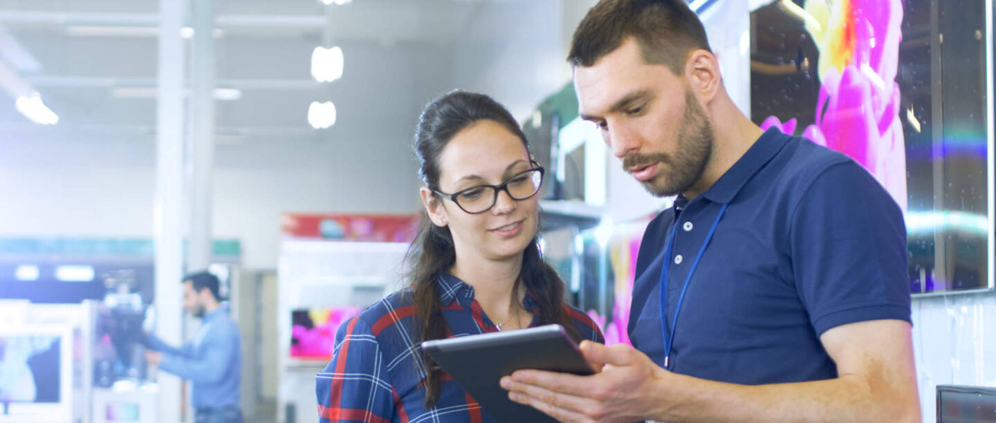 Een verkoopmedewerker bekijkt een tablet met een klant
