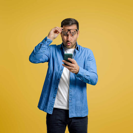 Een man kijkt verbaasd naar zijn mobiel telefoon.