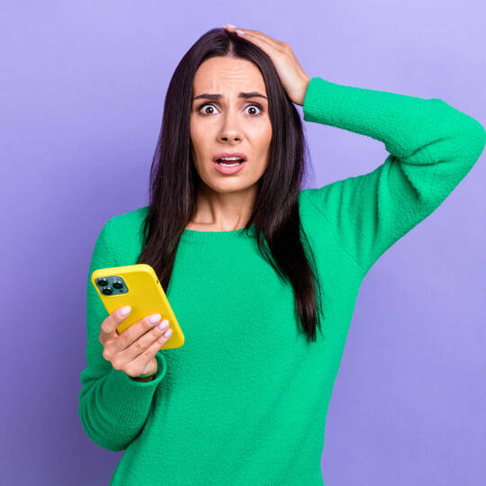 Een vrouw met smartphone in handen kijkt wanhopig in de camera.