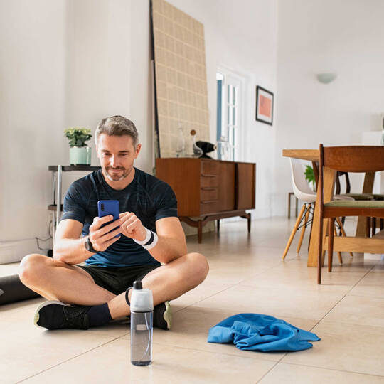 Een man in sportkleding zit op de grond met zijn smartphone in handen. 