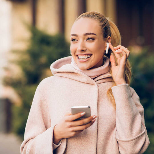 Vrouw heeft AirPods in haar oor en een smartphone in handen